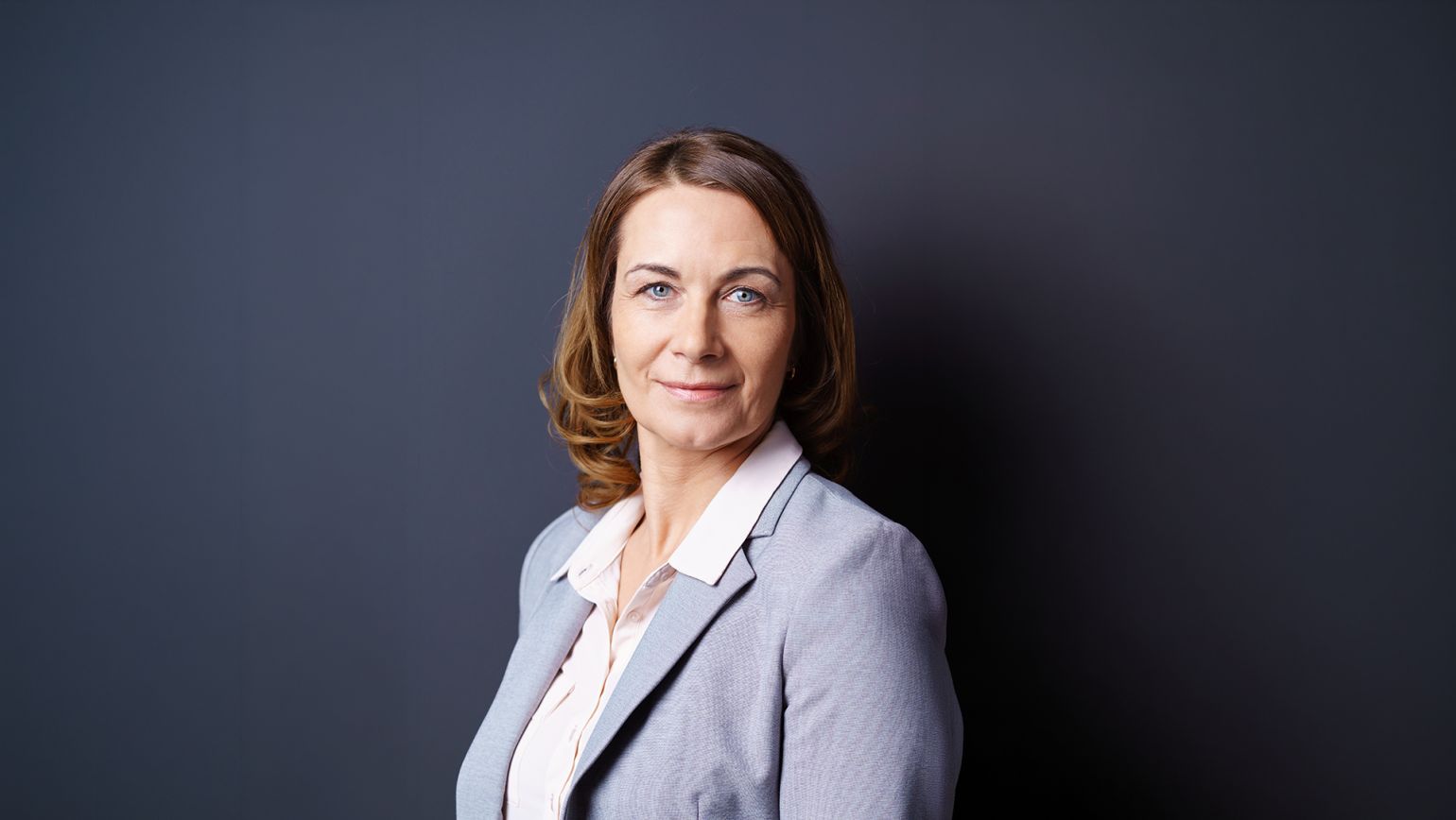 Studioaufnahme einer Business-Führungskraft vor dunkelgrauem Hintergrund, in hellgrauem Blazer und weißer Bluse, mit direktem Blick in die Kamera. Das klare, sachliche Porträt vermittelt Vertrauen, Kompetenz und Seriosität – ideal für B2B-Kommunikation in regulierten Branchen, Qualitätssicherung und Compliance. Studioaufnahme einer Business-Führungskraft vor dunkelgrauem Hintergrund, in hellgrauem Blazer und weißer Bluse, mit direktem Blick in die Kamera. Das klare, sachliche Porträt vermittelt Vertrauen, Kompetenz und Seriosität – ideal für B2B-Kommunikation in regulierten Branchen, Qualitätssicherung und Compliance.